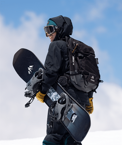 Ein Mann steht in einer verschneiten Berglandschaft und hält sein Jeremy Jones Board unterm Arm