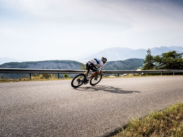 Ein Mann fährt auf einem Scott Addict Gravelbike eine Passtraße entlang im Hintergrund ist ein wolkenverhangenes Bergpanorama